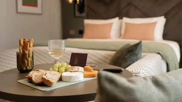 A neatly arranged breakfast table with bread, cheese, grapes, and a glass of white wine in a hotel room.