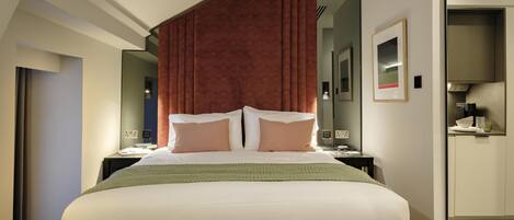 A modern hotel room with a large bed, a wooden headboard, a nightstand, a mirror, and a wardrobe.