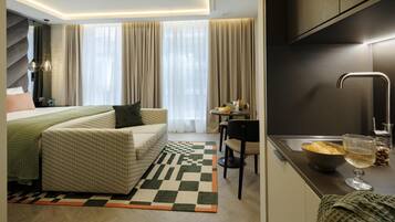 A modern hotel room with a bed, a sofa, a dining area, and a kitchen.