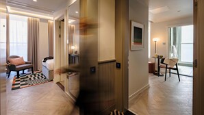 A modern hotel room with a large mirror, a bed, a sofa, and a dining area with a table and chairs.
