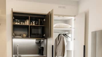 Een compacte kitchenette met een koffiezetapparaat, een magnetron en bergplanken.