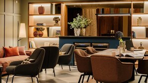A modern living room with a sofa, armchairs, a dining table, and a kitchen area with a built-in oven and microwave.