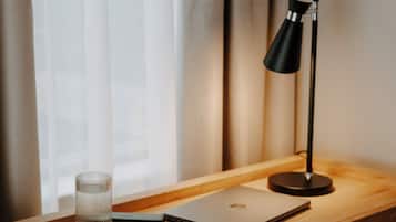 A wooden desk with a laptop, a glass, and a black desk lamp.
