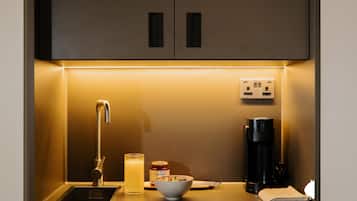 Una cocina con un lavamanos, una cafetera, un tazón de cereales y un tarro de mermelada.