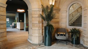 Una hall con un’imponente scalinata, una reception e un’area salotto con una poltrona moderna e piante in vaso.