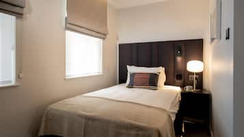 A neatly made bed with a beige bedspread, a striped pillow, and a bedside lamp.