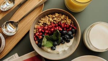 A breakfast setting with a bowl of yogurt topped with berries, a glass of orange juice, a croissant, and a newspaper.