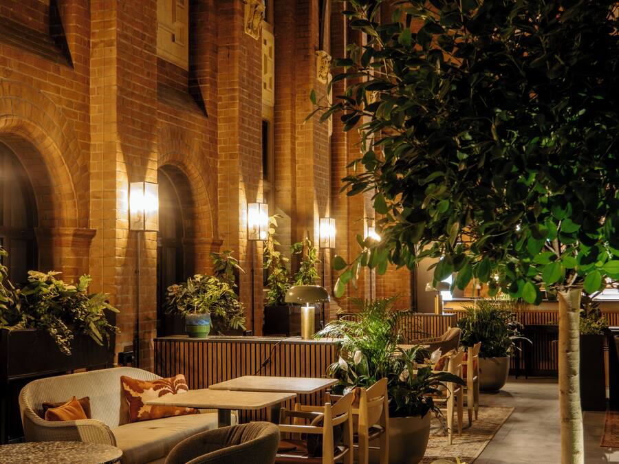 An indoor courtyard with brick walls, arched windows, and a variety of seating arrangements including tables and chairs.