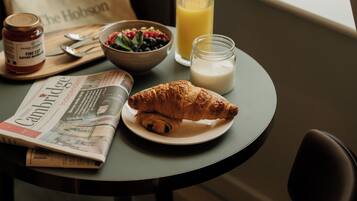 A breakfast setting with a croissant, bowl of fruit, glass of orange juice, milk, and a bag of The Hobson.