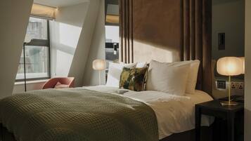 A hotel room with a bed, a chair, a nightstand, and a window with curtains.