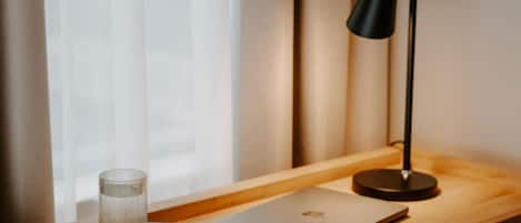 A laptop on a wooden desk with a black lamp and a clear glass beside it.