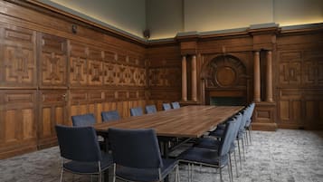 A conference room with a long wooden table, blue upholstered chairs, and ornate wooden paneling.