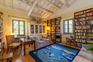 A cozy reading room with a fireplace, bookshelves, a plaid sofa, and a large rug.