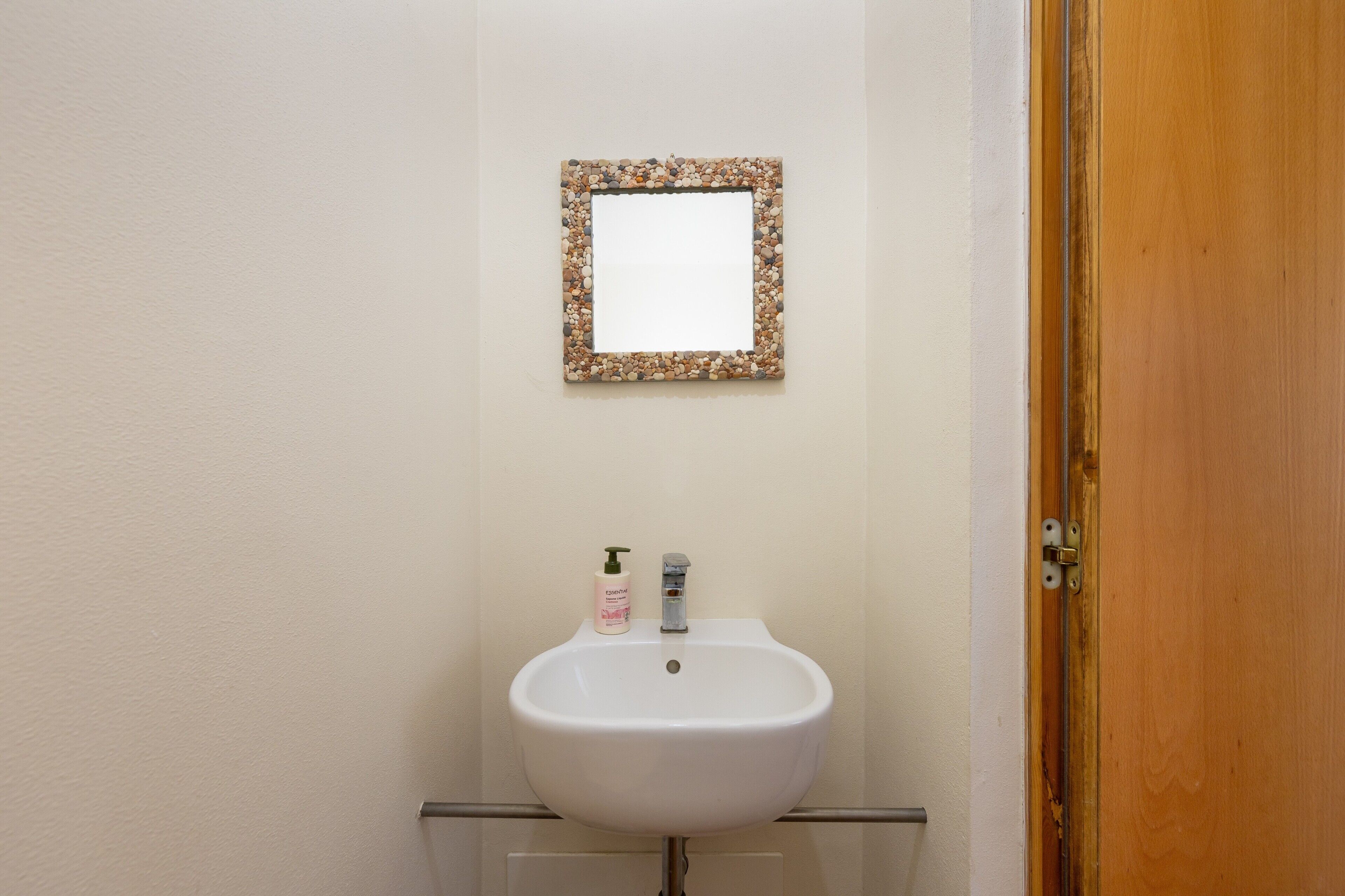 Un baño con lavamanos blanco, un espejo con marco decorativo y una botella de jabón para manos.