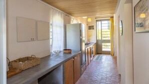 A kitchen with a wooden ceiling, a refrigerator, a sink, and a window with curtains.