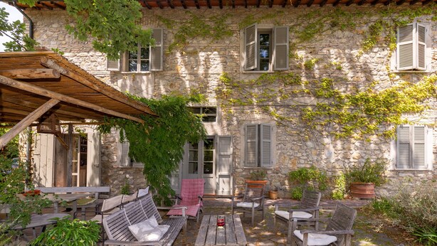 A stone building with ivy, wooden furniture, and a pergola.