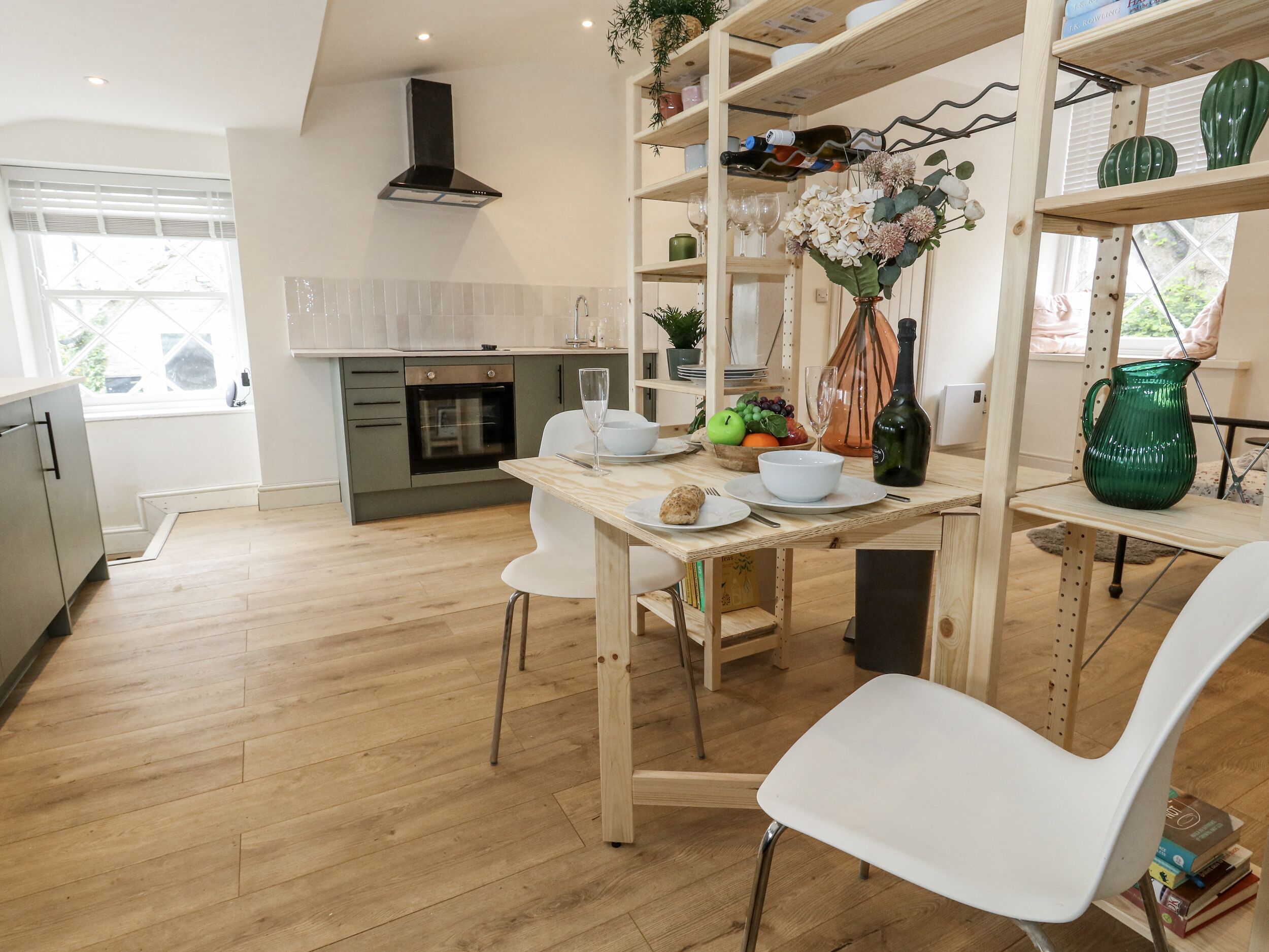 Une cuisine moderne avec un plancher en bois, un four encastré et un coin repas comprenant des chaises blanches et une table en bois.