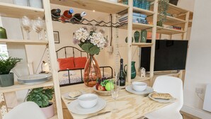 Un'area pranzo con un tavolo di legno, sedie bianche, un vaso con fiori e una libreria con diversi oggetti.