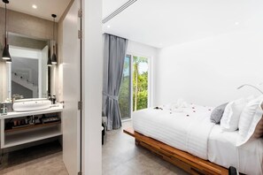 Un dormitorio moderno con una cama grande, una tocador con espejo y vistas a la vegetación por la ventana.