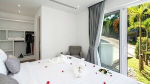 A modern hotel room with a large bed, a walk-in closet, and a view of a tropical garden.