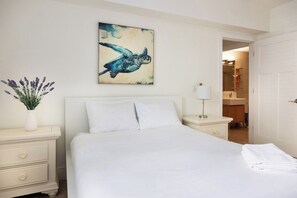 A hotel room with a bed, a nightstand with a lamp, a painting of a sea turtle, and a vase with flowers. - Luxe 3BR Apartment with Great Patio at Yacht Club (Aventura)
