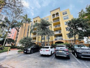 A multi-story residential building with balconies, parked cars, and surrounding greenery. - Luxe 3BR Apartment with Great Patio at Yacht Club (Aventura)