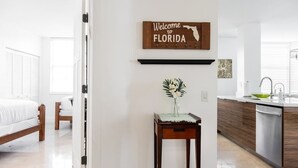A modern bedroom with a bed, a bedside table with a vase, and a wall-mounted sign reading "Welcome to Florida". - Luxe 3BR Apartment with Great Patio at Yacht Club (Aventura)