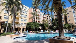 Une piscine d’hôtel entourée de palmiers, de chaises longues et surplombée d’un ciel bleu azur.