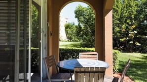 Une terrasse avec une table ronde et des chaises, une arche et, en arrière-plan, une vue sur un jardin et un bâtiment.