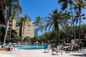 A pool area with lounge chairs, palm trees, and a building in the background. - Luxe 3BR Apartment with Great Patio at Yacht Club (Aventura)