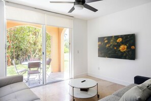 A living room with a sofa, a coffee table, a ceiling fan, and a sliding glass door leading to an outdoor area with a patio table and chairs. - Luxe 3BR Apartment with Great Patio at Yacht Club (Aventura)