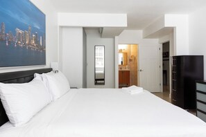 Une chambre d’hôtel avec un lit, une grande fenêtre, une armoire et une salle de bain visible à travers une porte ouverte.