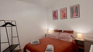 A neatly arranged bedroom with a bed, two bedside tables, a hanging rack, and three wall-mounted artworks.