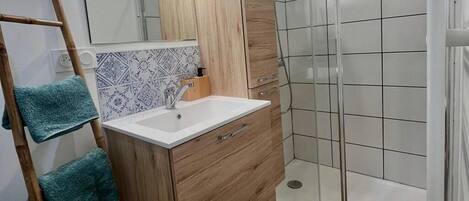 A bathroom with a wooden vanity, a white sink, and a shower area.