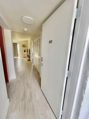 A hotel corridor with a wooden floor, a door labeled '202', and a ceiling light.
