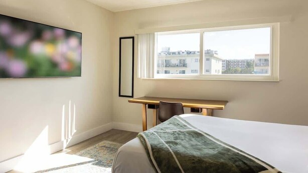 Ein Hotelzimmer mit Bett, Schreibtisch und großem Fenster mit Blick auf die Stadt.