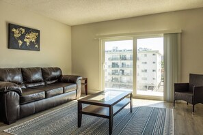 A living room with a leather sofa, a glass coffee table, and a view of a building through a large window.