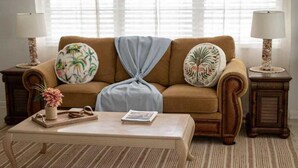 A cozy living room with a brown sofa, two decorative pillows, a blue throw, a wooden coffee table with a magazine, and two lamps on side tables.
