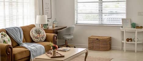 A living room with a brown sofa, a white coffee table, a grey armchair, a wicker basket, and a white side table.