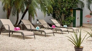 A row of beige lounge chairs with colorful pillows, a small green shed, and a flamingo mural on the wall.