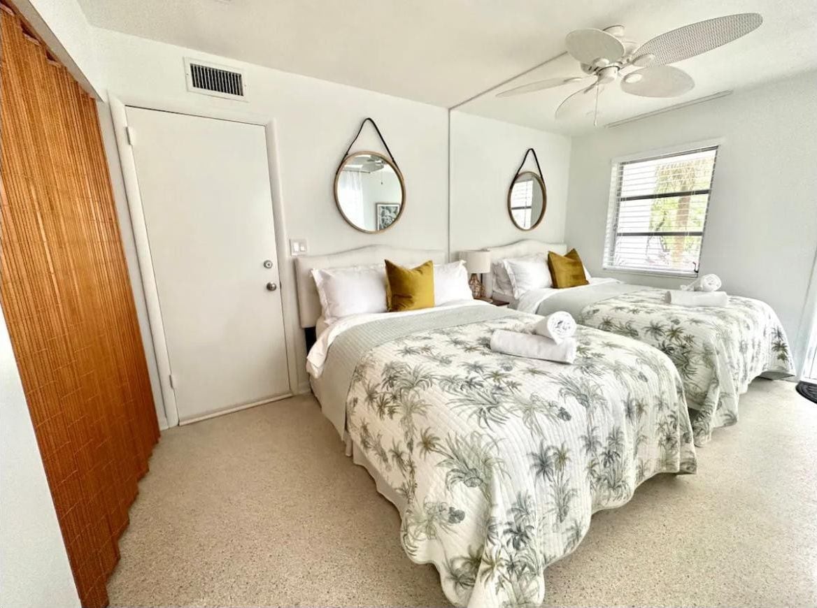 A bedroom with two beds, a ceiling fan, and a window with blinds.