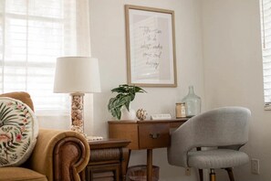 Um quarto aconchegante com uma escrivaninha de madeira, uma cadeira cinza, um abajur, uma planta em vaso e uma frase motivacional na parede.