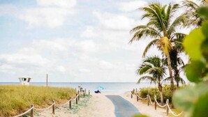 Une promenade bordant la plage, avec un poste de surveillance pour les sauveteurs, des palmiers et une personne assise sous un parasol.