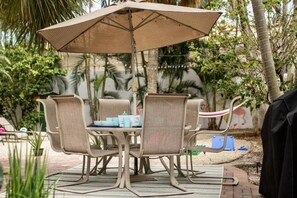 Een terras buiten met een tafel en stoelen, omgeven door groen en een muurschildering.