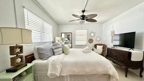 Une chambre à coucher avec un lit, une commode, un téléviseur et un ventilateur de plafond.