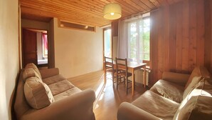 Ein Zimmer mit Holzwänden und -decke, einer Couch, einem Esstisch mit Stühlen und einem Fenster mit Vorhängen.