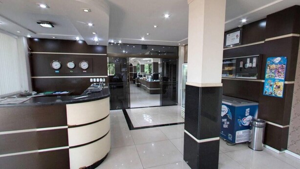 A modern reception area with a curved reception desk, a clock, and a poster on the wall. - Samambaia Hotel (Foz do Iguaçu)