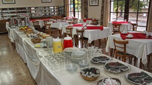 Montaje tipo bufé con varias mesas, cada una cubierta con mantel blanco y servilletas rojas, mostrando una variedad de alimentos y cristalería.
