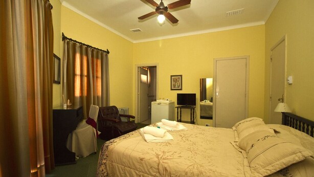 Habitación de hotel con cama, escritorio, silla, ventilador de techo y puerta.