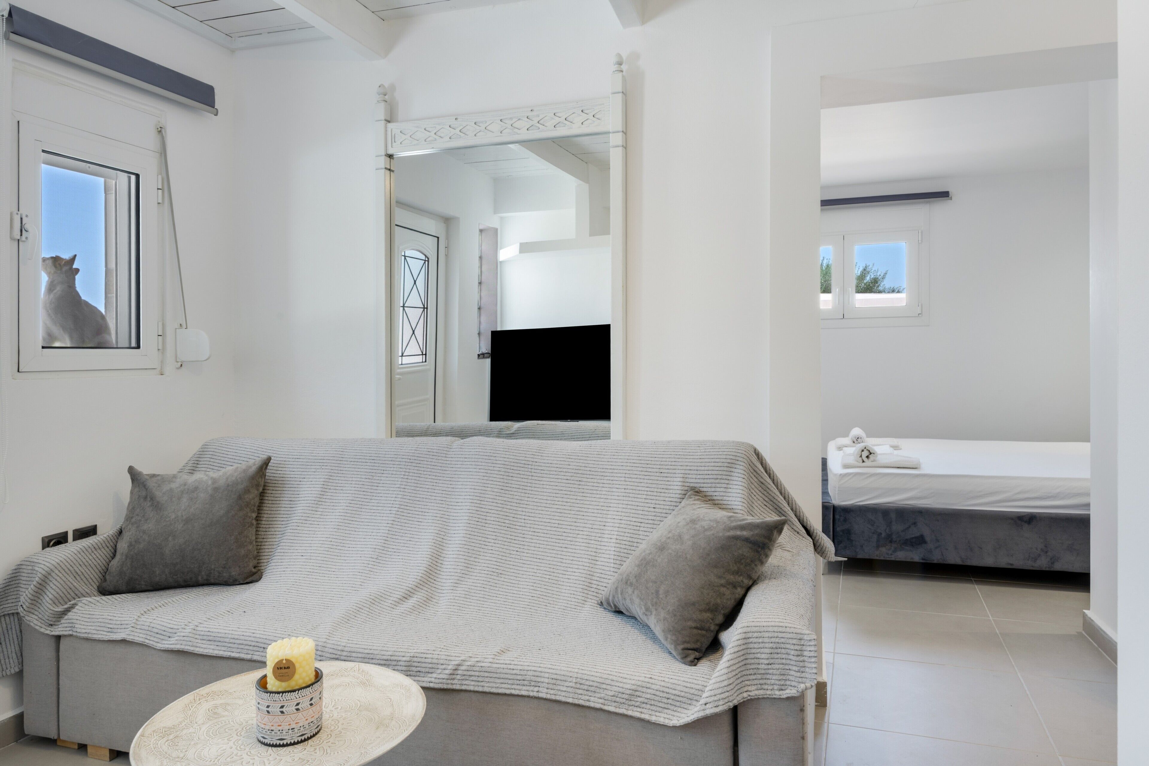A modern room with a sofa, a small round table with a candle, a bed, and a TV.